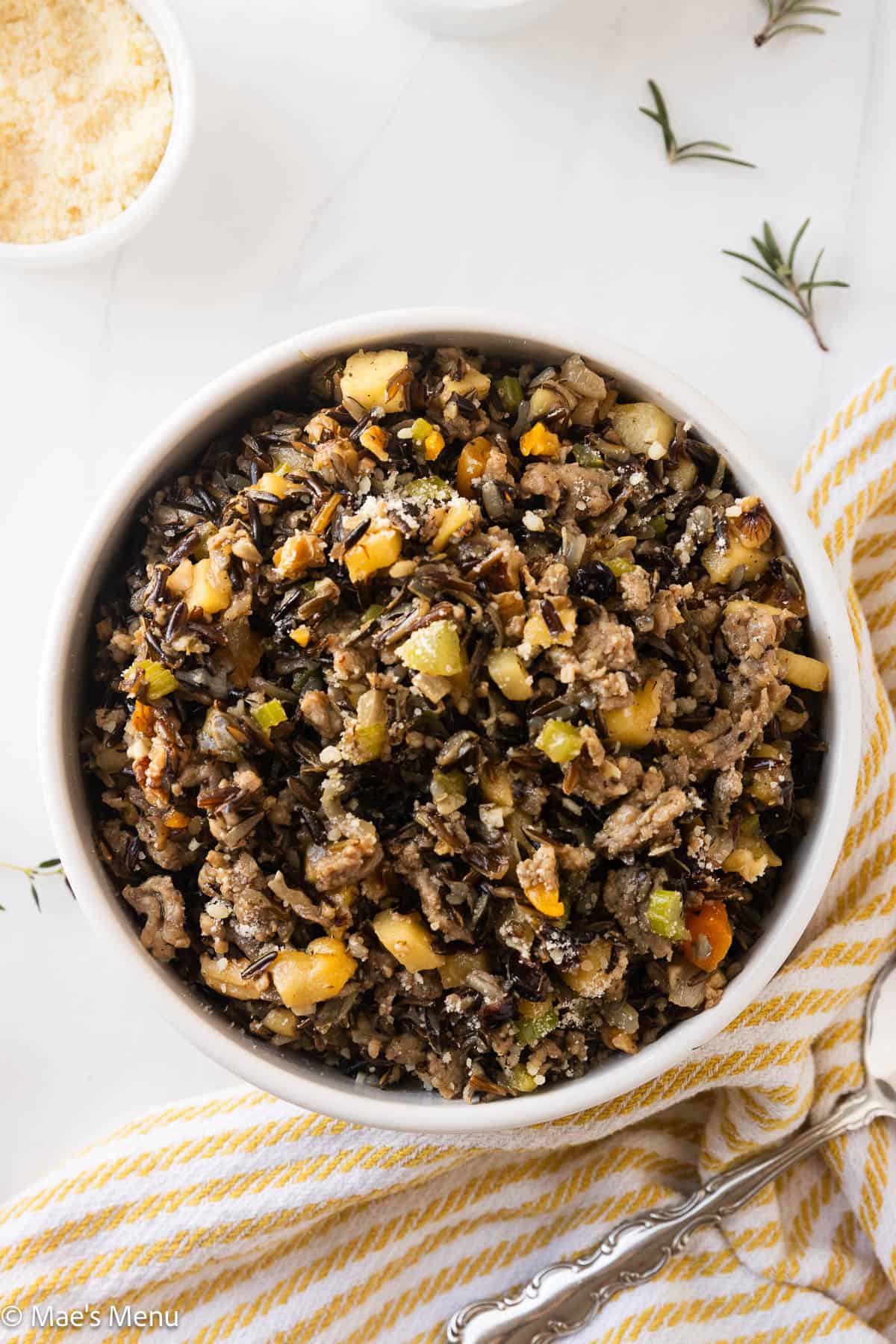An overhead shot of a serving bowl of wild rice stuffing on the counter with herbs and a dish.