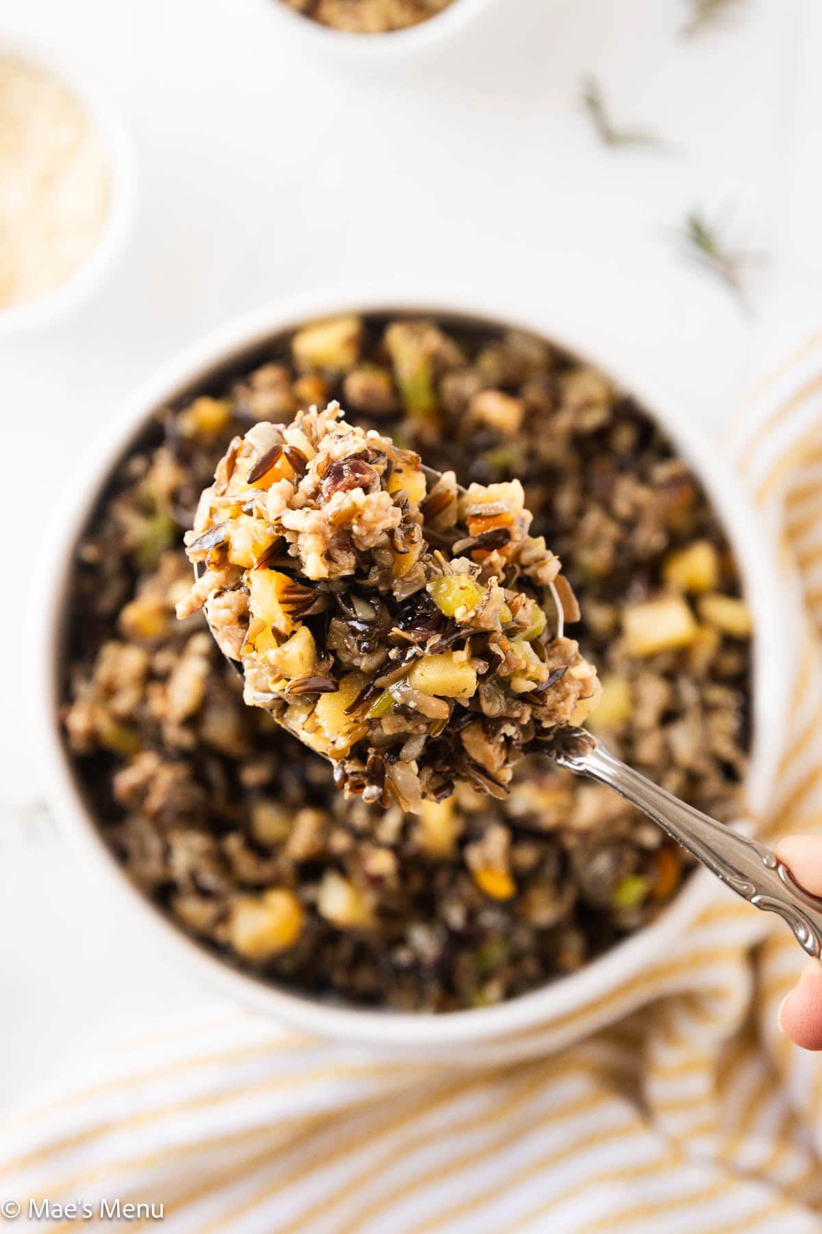 A close-up overhead shot of a spoonful of wild rice seasoning over the serving bowl.