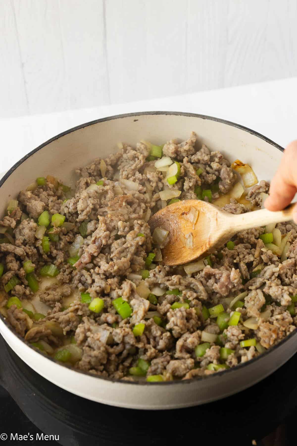 Stirring the sausage and veggies in a white skillet.