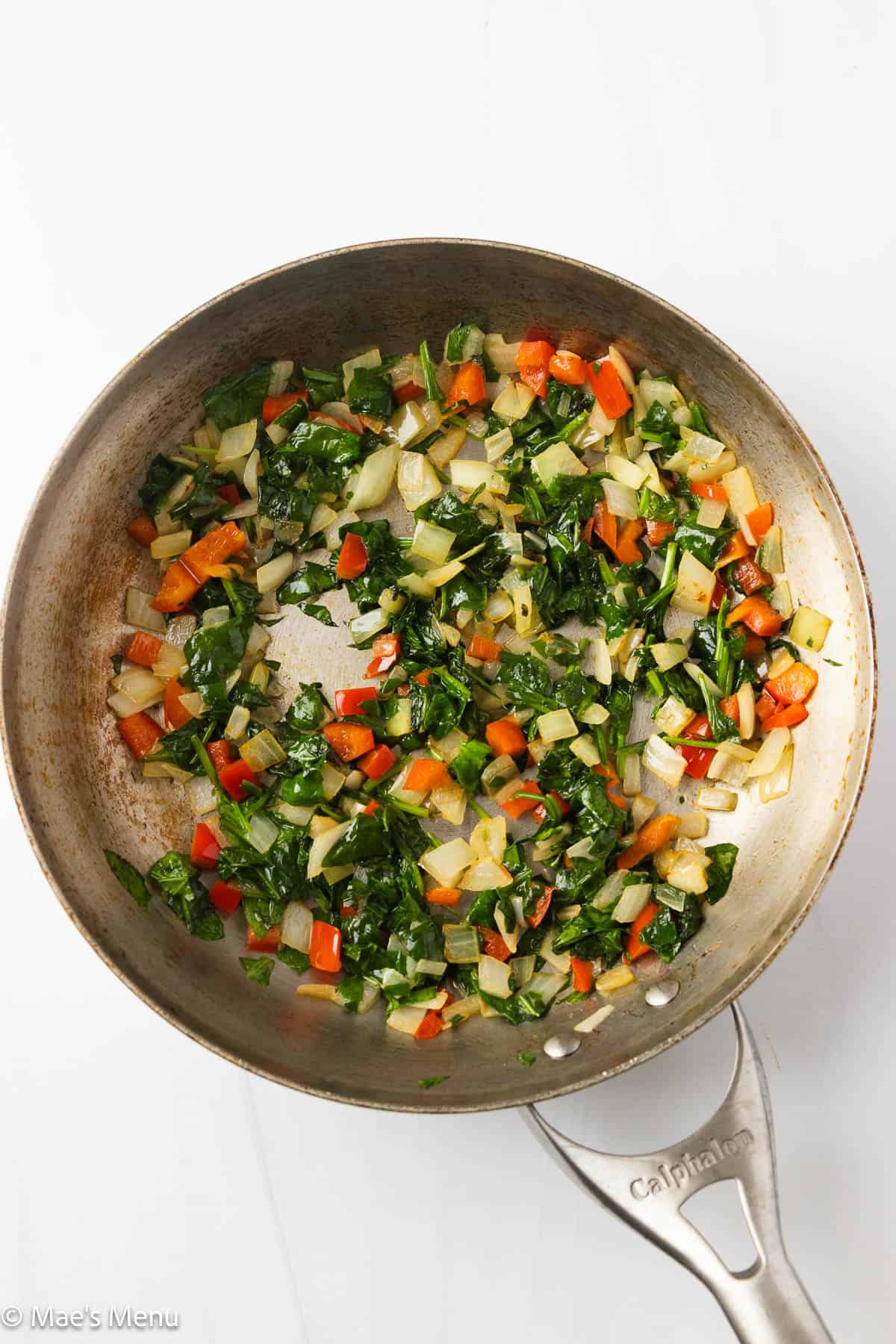 Sautéed onions, peppers, and spinach in skillet.