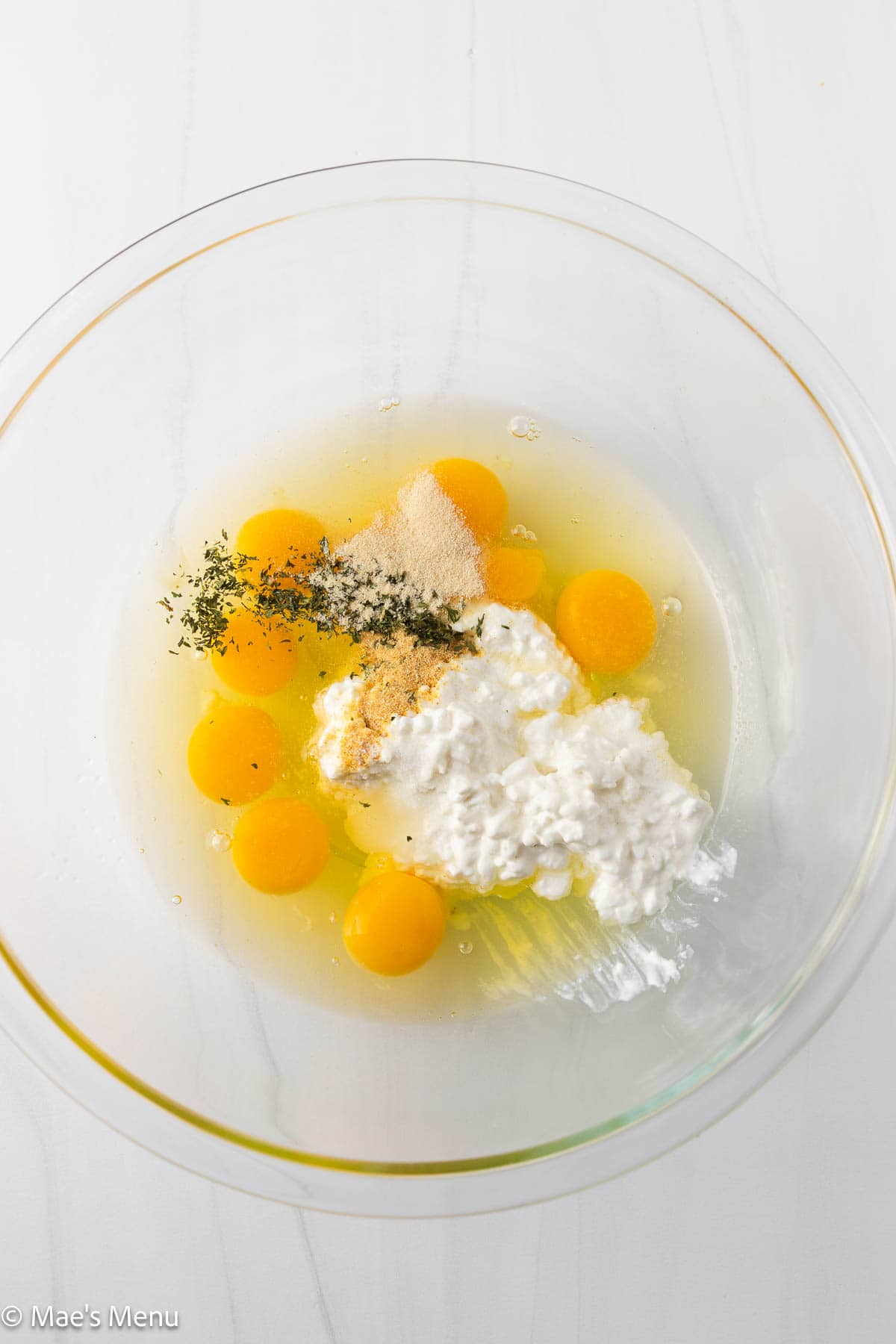 A large mixing bowl with eggs, cottage cheese, and seasonings.