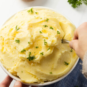 An overhead shot of two hands serving cream cheese potatoes.