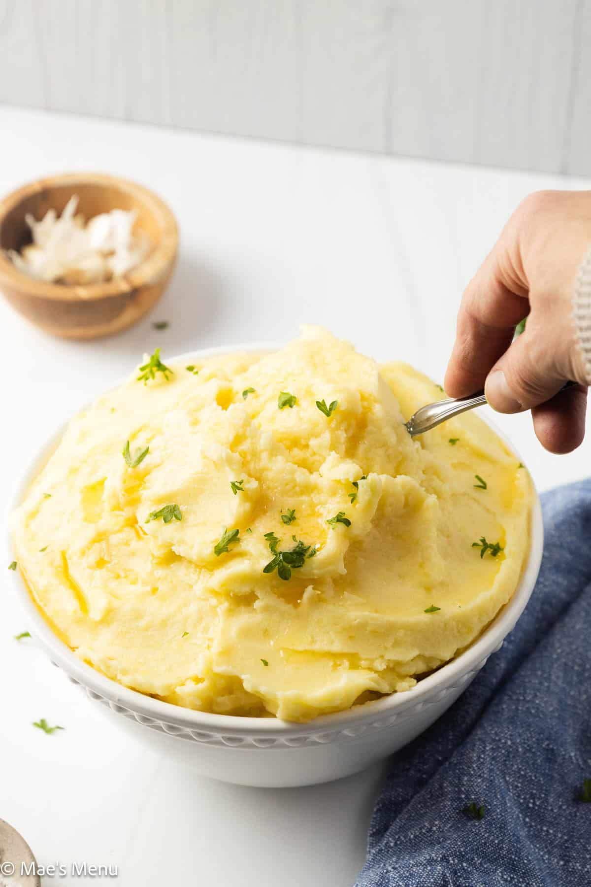 A hand going for a scoop of cream cheese mashed potatoes.