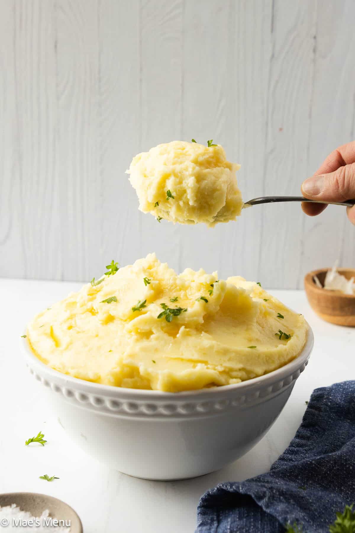A side shot of a scoop of the mashed potatoes over the serving bowl.