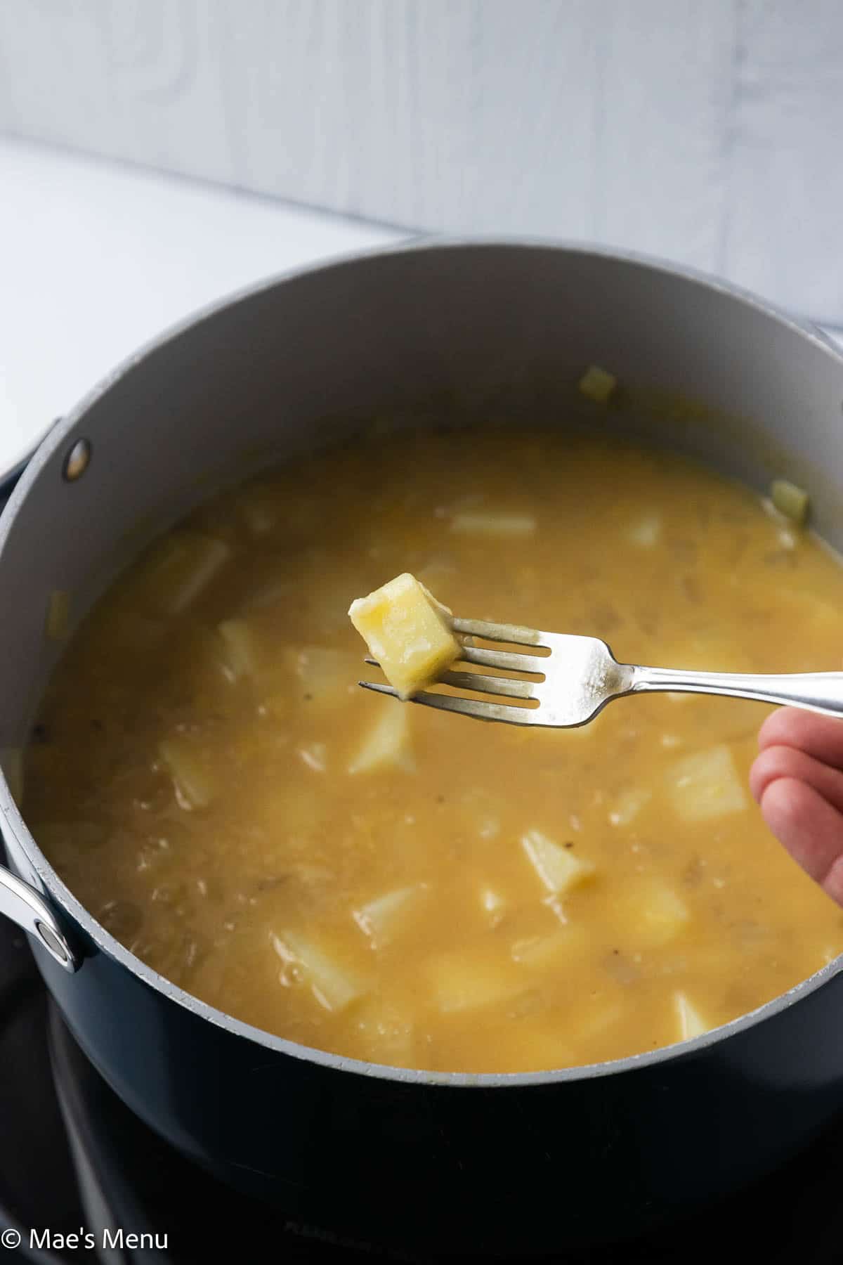 Piercing a fork over the pot of simmered potato soup