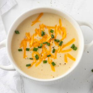 An overhead shot of a bowl of cottage cheese potato soup, topped with cheddar cheese and chives.