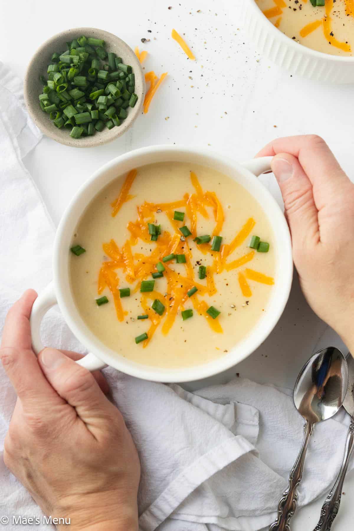 Two hands holding a bowl of potato soup with protein.