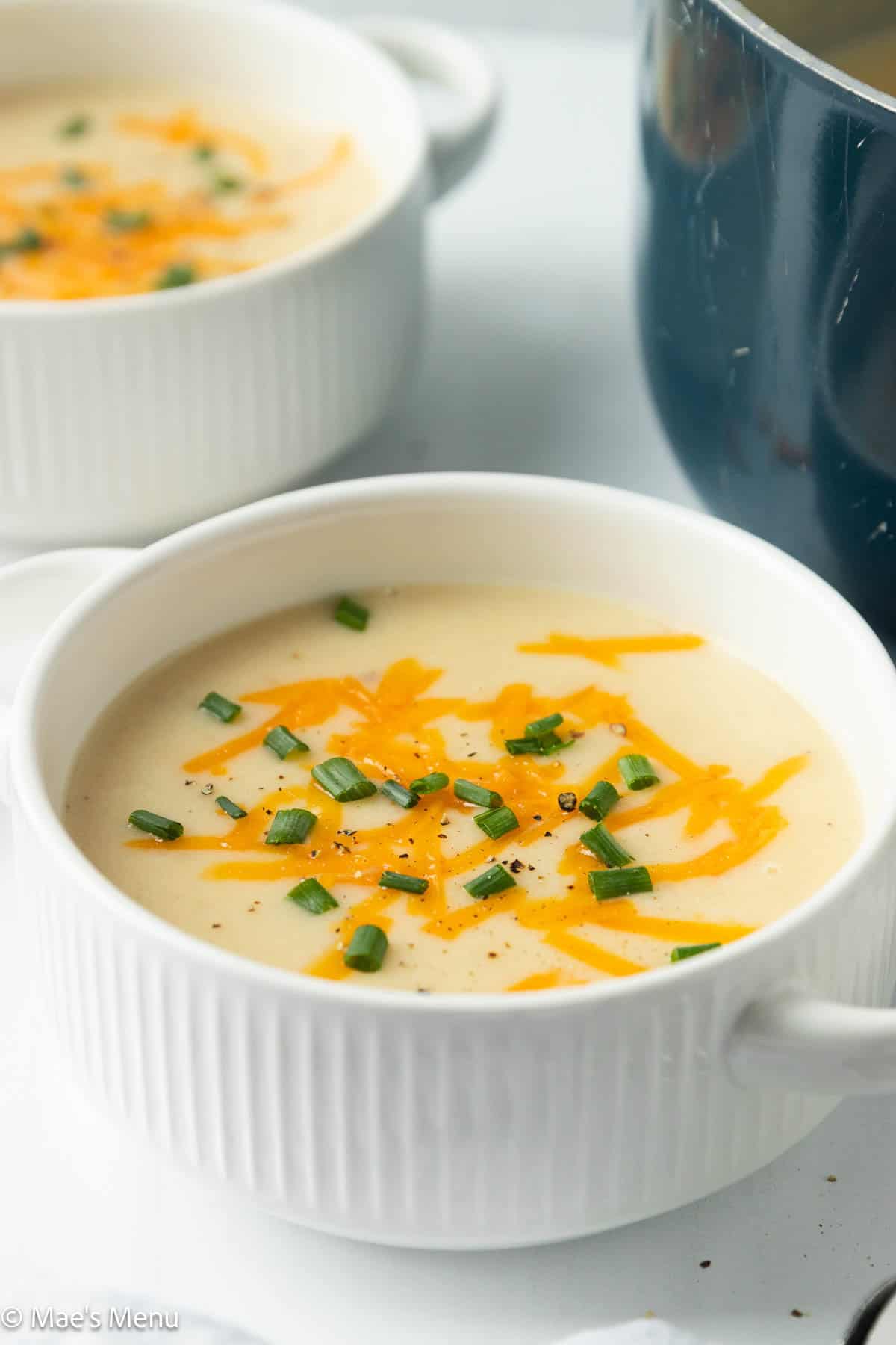 A close-up angled shot of a bowl of healthy high protein potato soup, topped with cheese and chives.