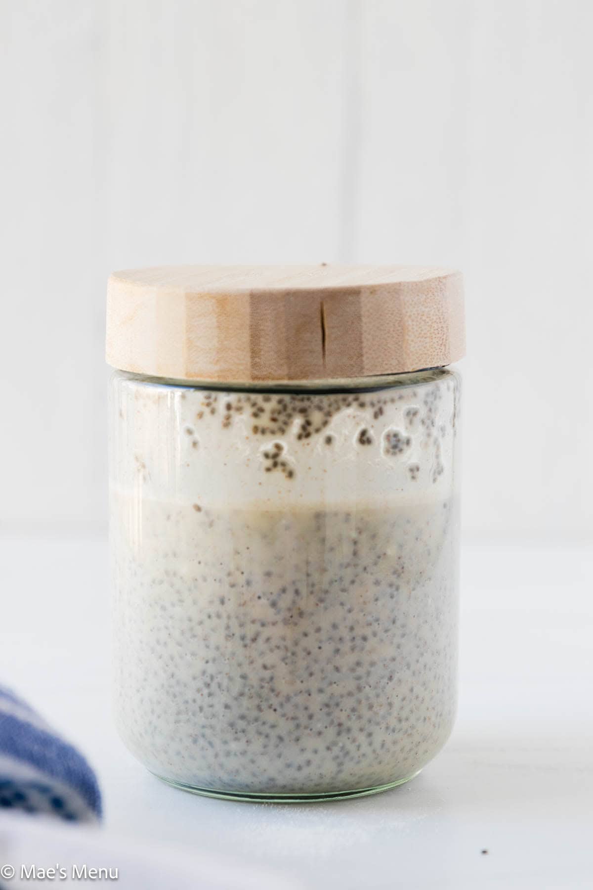 A side shot of a glass jar of protein chia seed pudding before setting. 