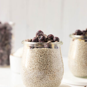 A close-up side shot of a cup of protein chia pudding topped with berries and chocolate chips.
