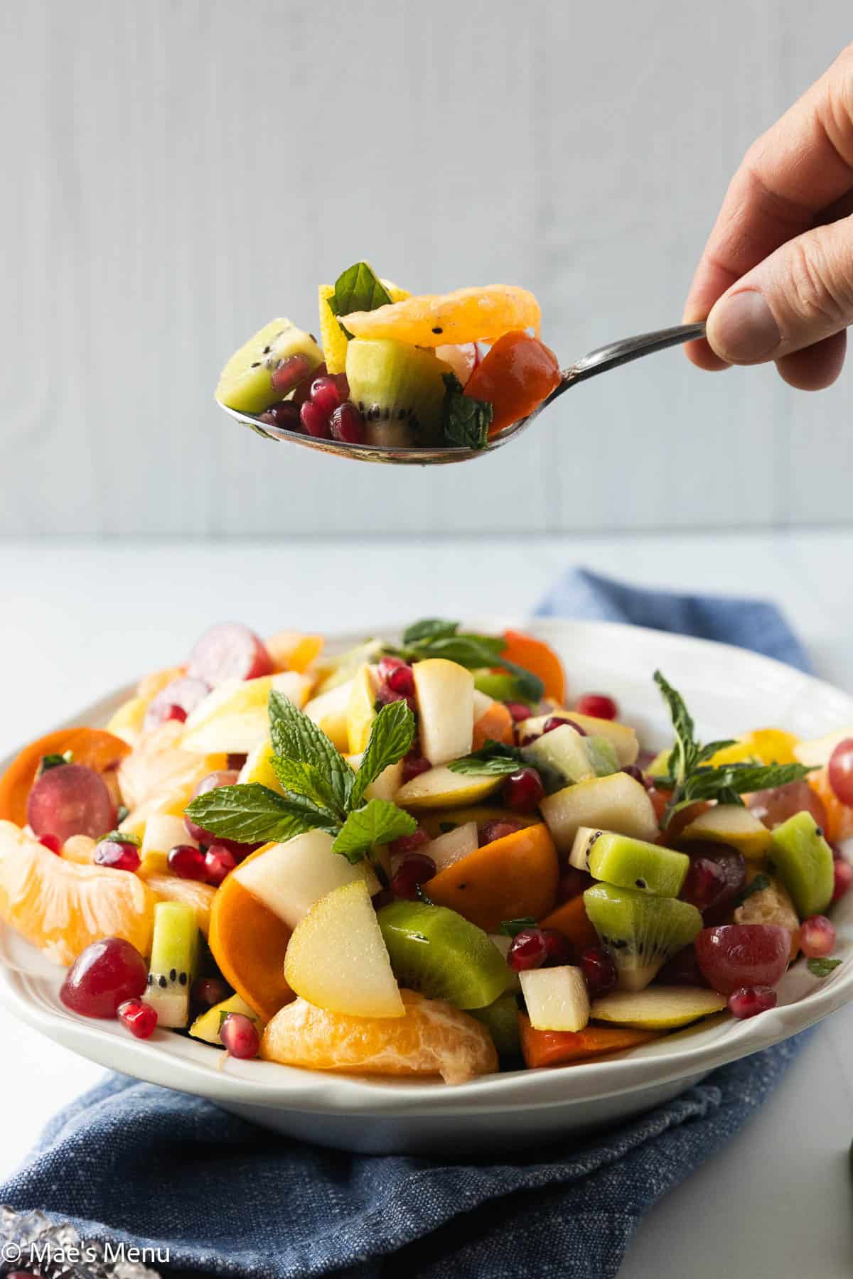 A hand holding a spoonful of winter fruit salad over the serving bowl.