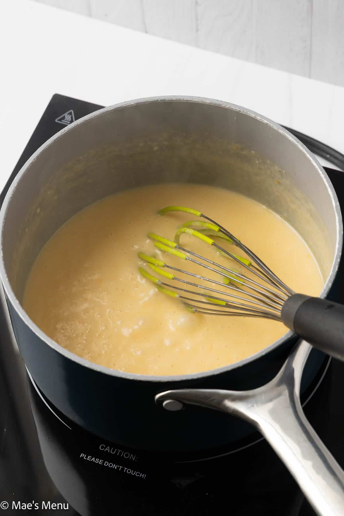 The 3 cheese mac and cheese sauce pin a saucepan with a whisk.