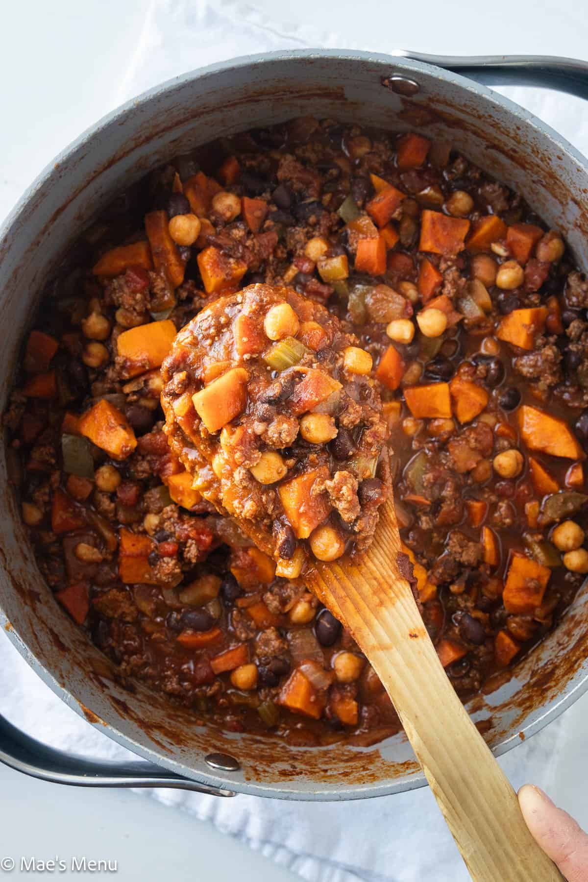 An overhead shot of a hand holding a wooden spoon of the bison chili.