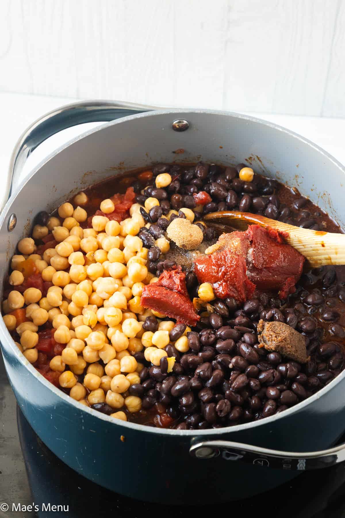 Adding all the ingredients to a large pot with a wooden spoon.