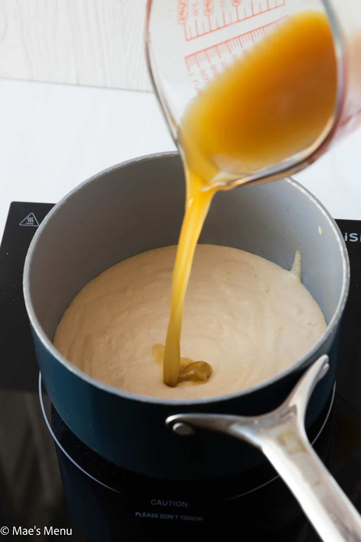 Pouring the bone broth into the pot with the blended cheese sauce mixture.