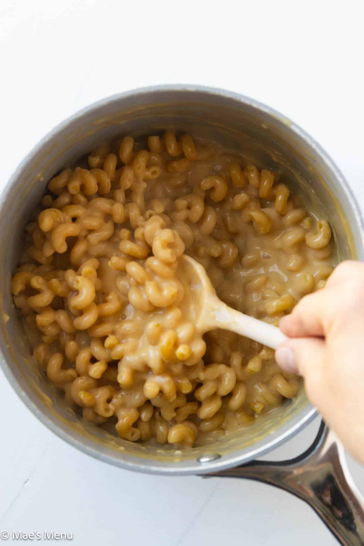 An overhead shot of a hand stirring a pot of high protein mac and cheese.