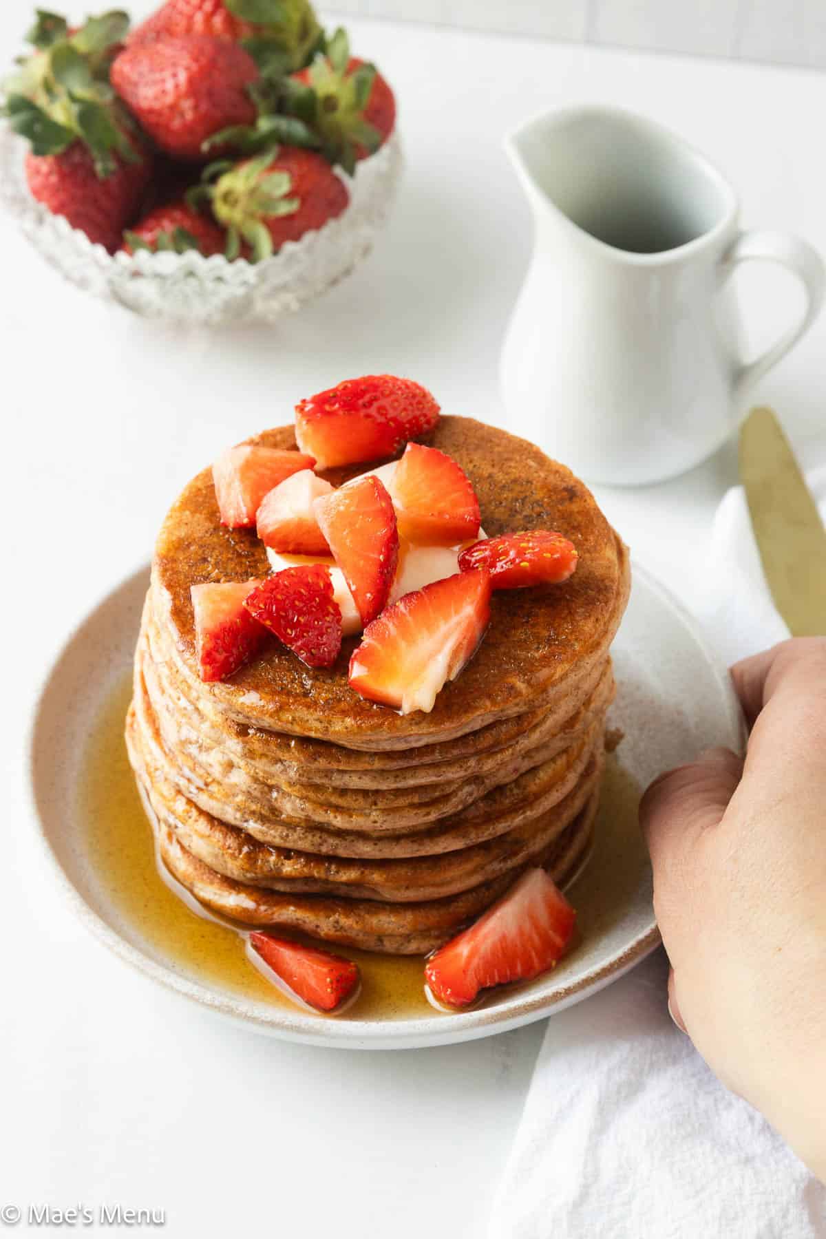 A hand holding a small dish of strawberry pancakes drizzled in maple syrup. 