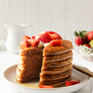 A side shot of a stack of strawberry protein pancakes with a wedge taken out of it.
