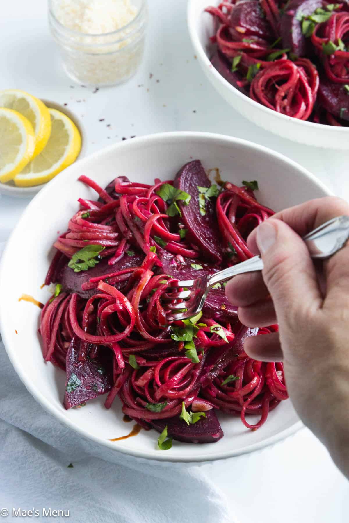 A hand twirling the pink pasta with beets in a white bowl.