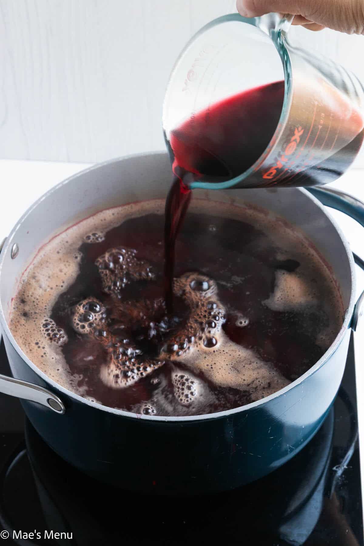 Pouring red wine into a pot of simmering beets.