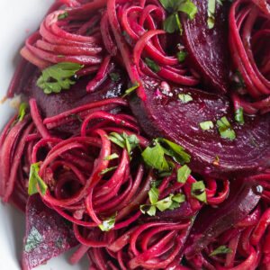 A close-up shot of pink pasta with beets in a bowl, topped with parsley.