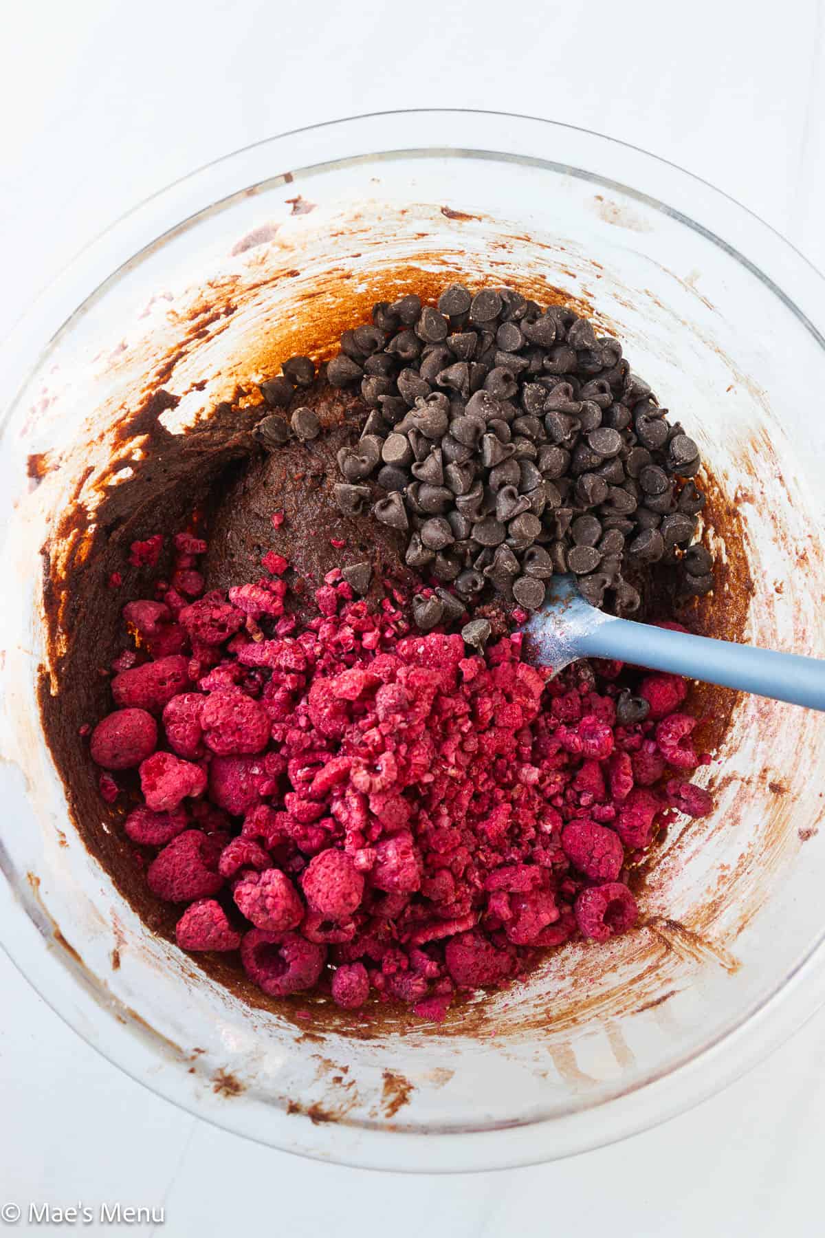 An overhead shot of a bowl of brownie batter with the dehydrated raspberries and chocolate chips.