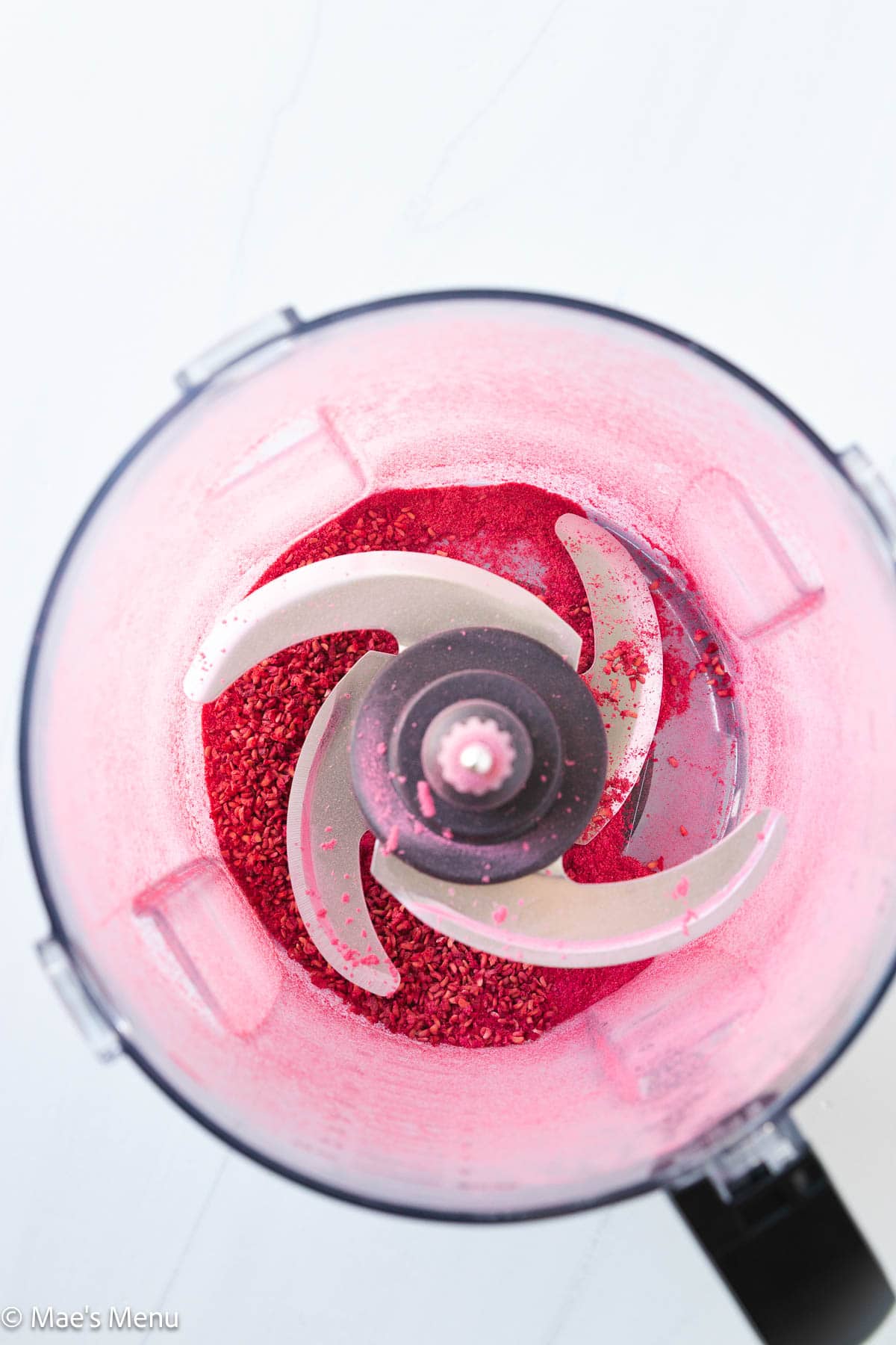 An overhead shot of dehydrated raspberry powder in a food processor.