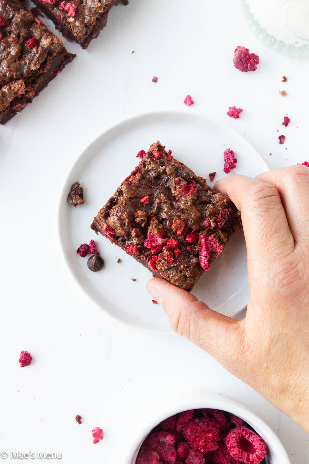 A hand grabbing a raspberry brownie on a small plate.