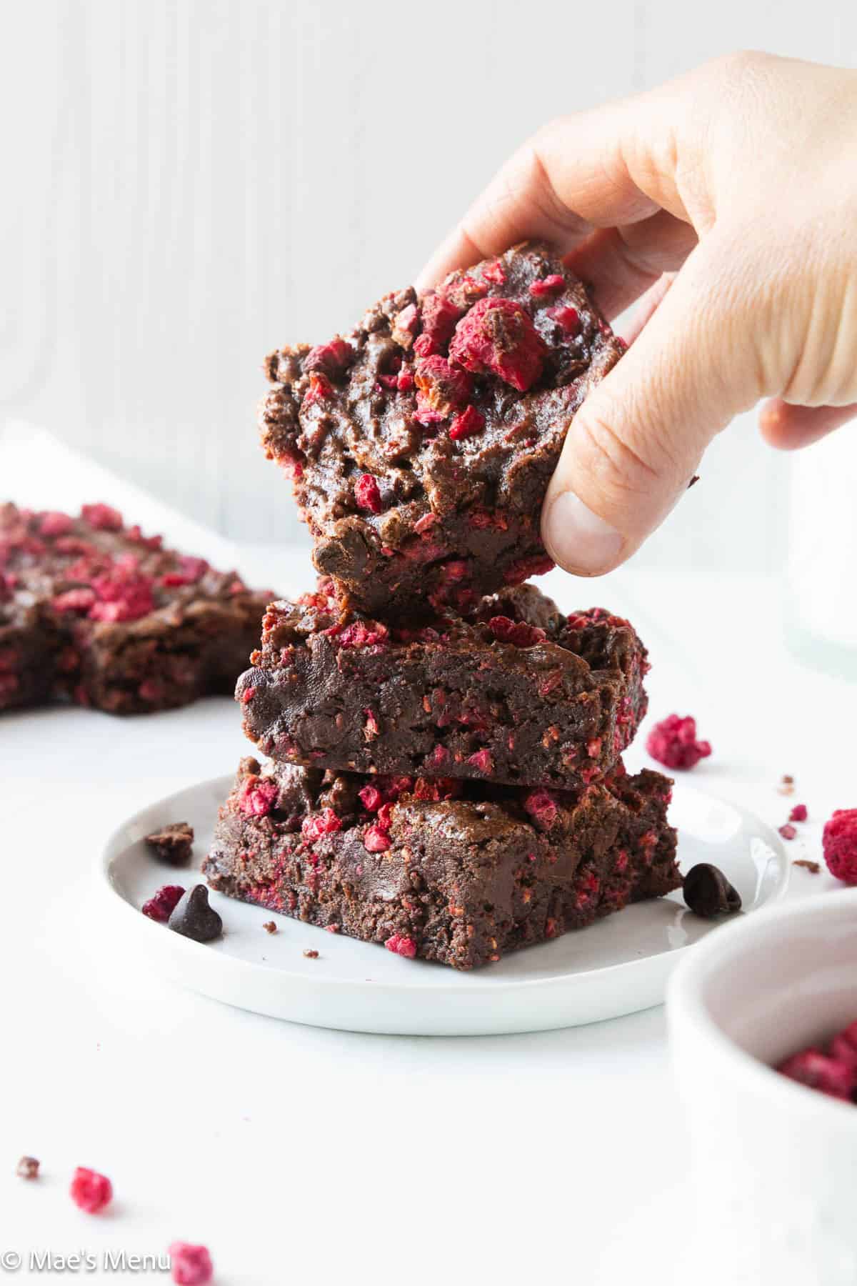 A hand taking a raspberry brownie off a tall stack.