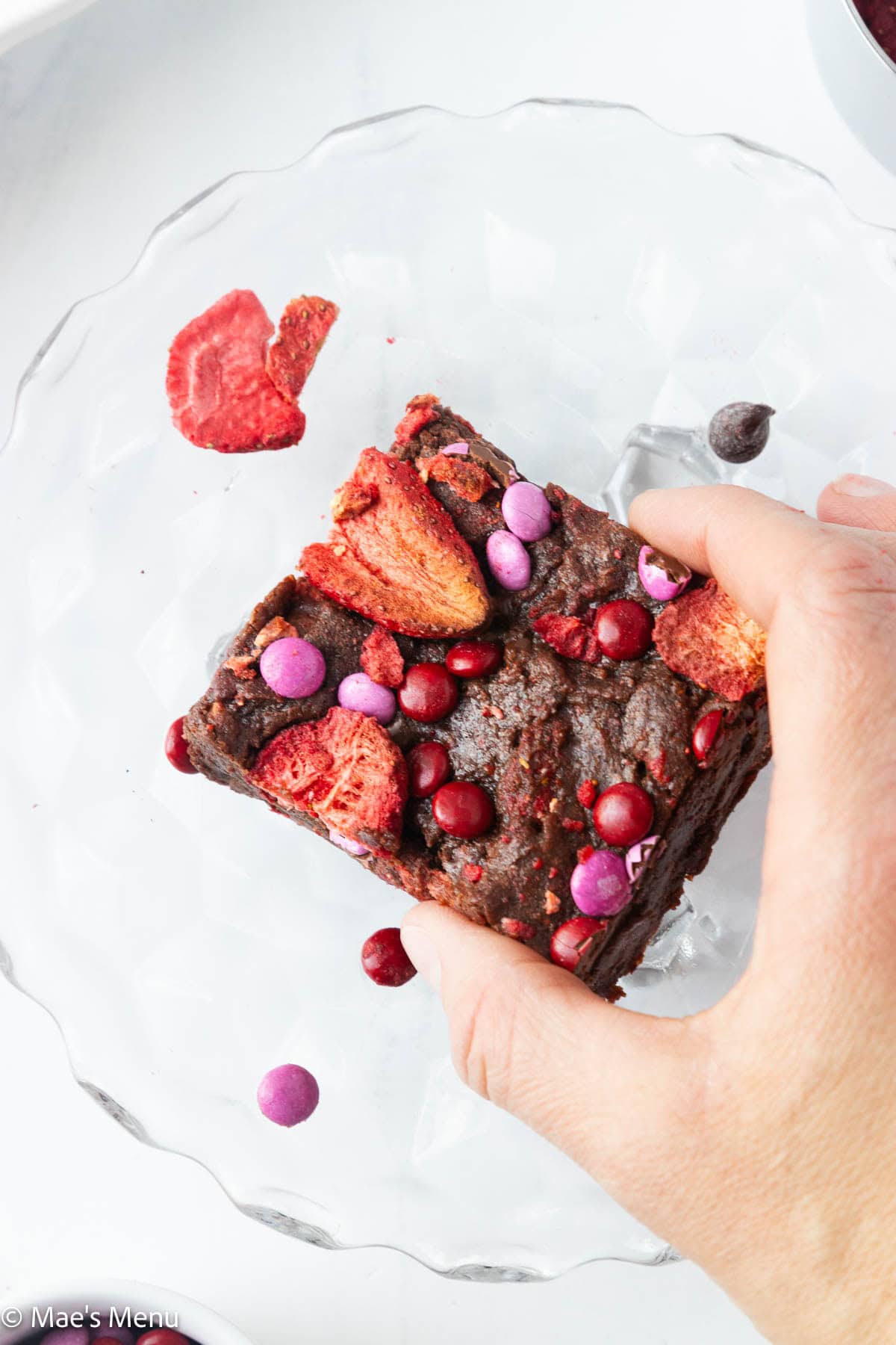 A hand grabbing a square of strawberry brownie.