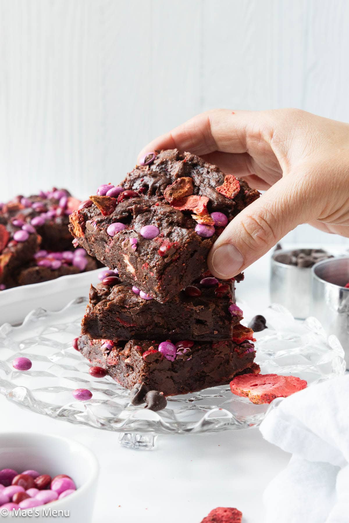 A hand grabbing a strawberry brownie off the top of the stack.