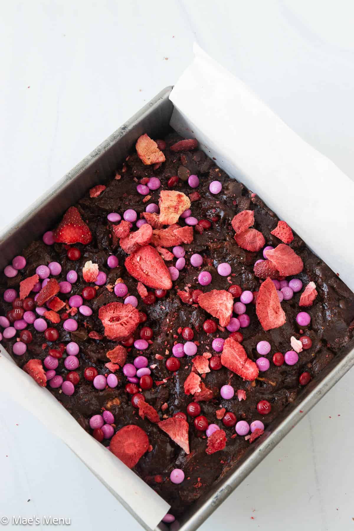 Adding the m&ms and freeze-dried strawberries to the pan of brownies before baking.
