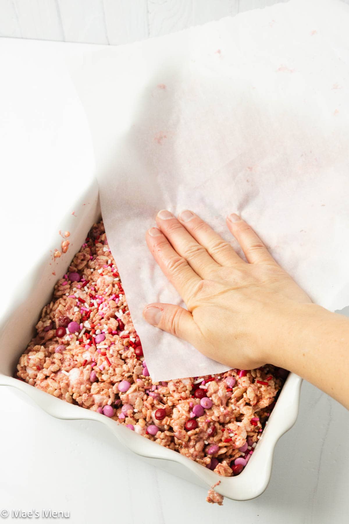 Hand pressing the rice krispies down with parchment paper.