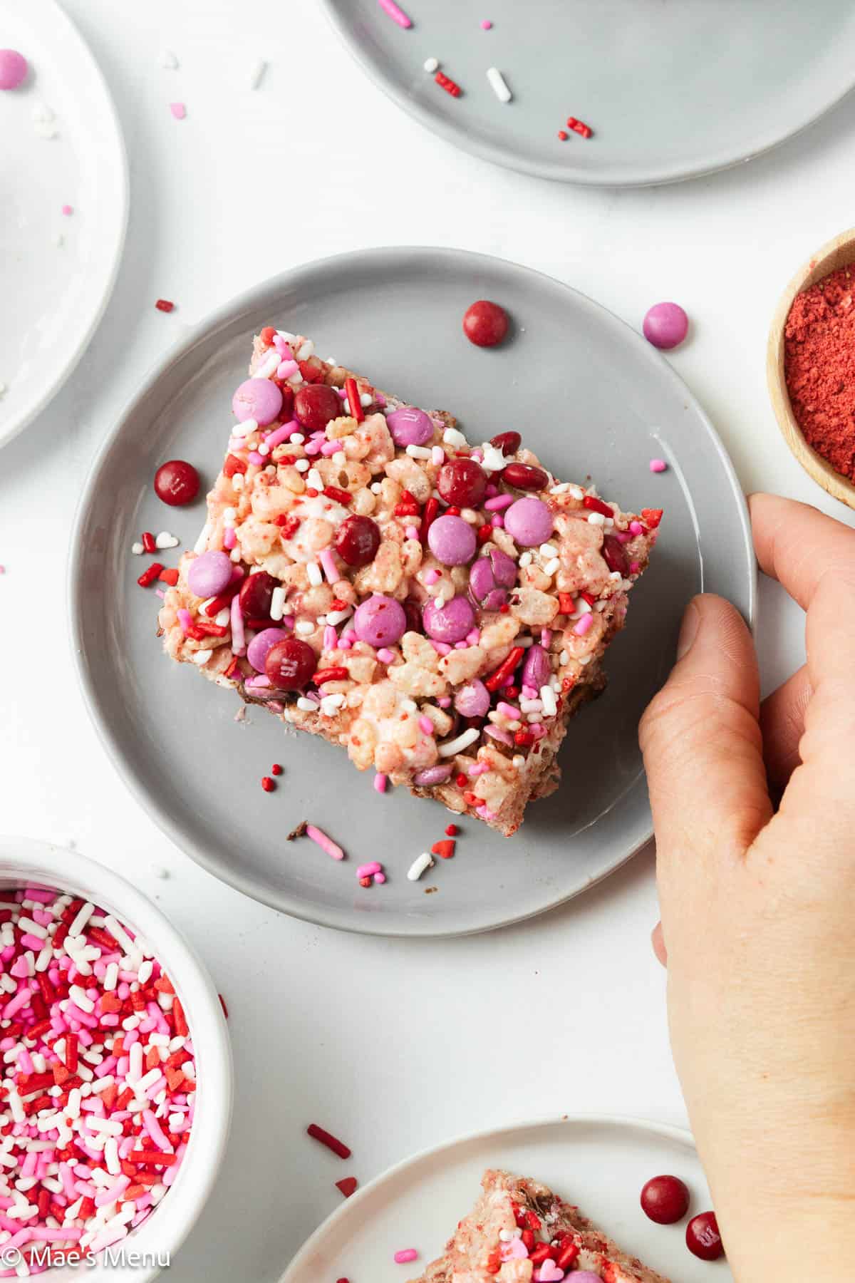 A hand grabbing a small plate of strawberry rice krispies.
