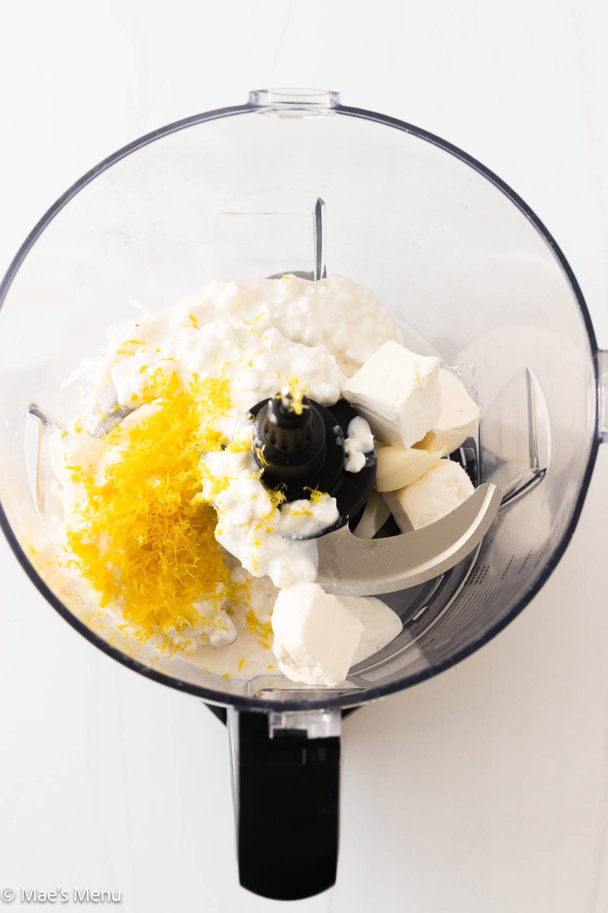 An overhead shot of the cottage cheese, lemon zest, garlic, salt, and cream cheese in the food processor bowl.