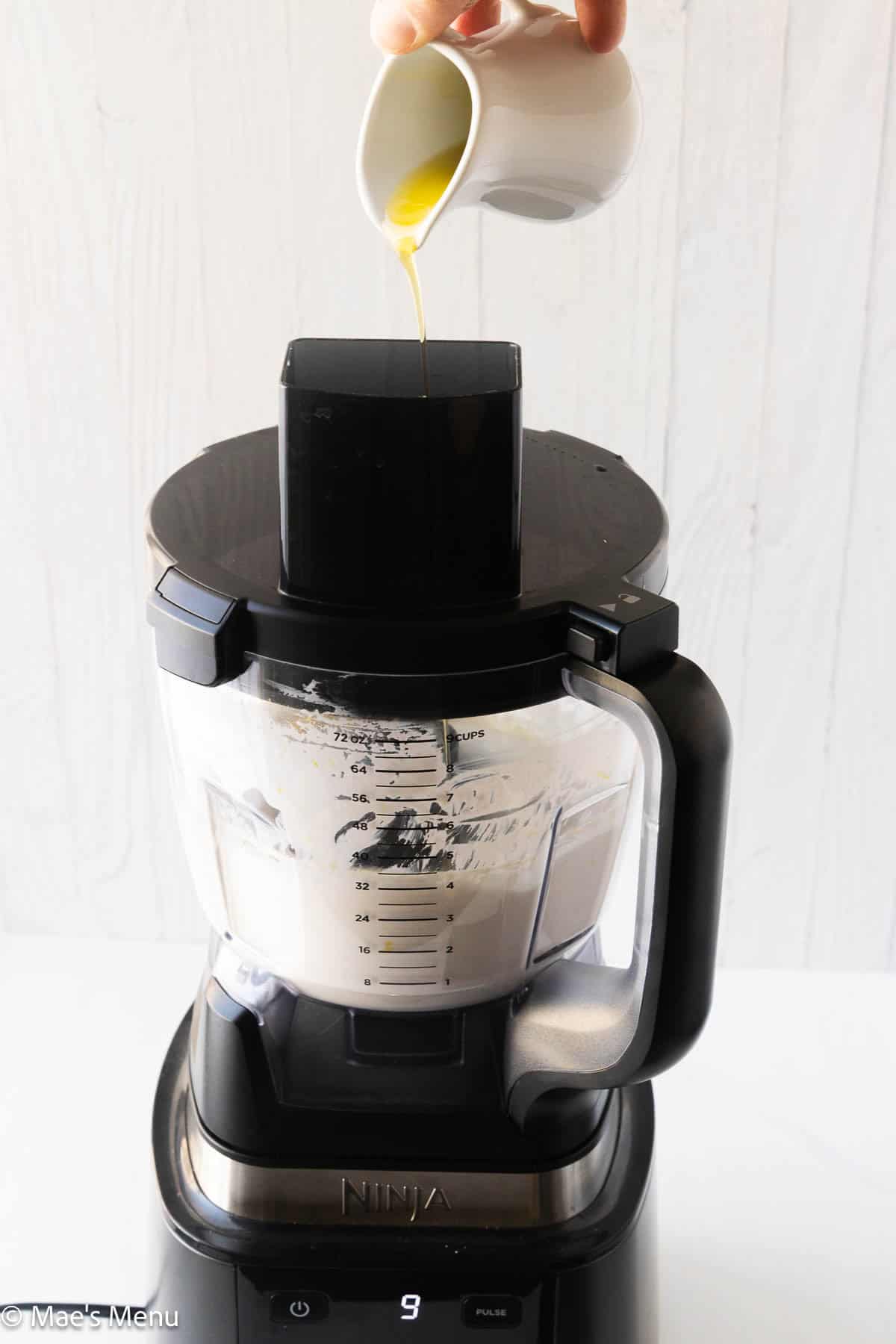 Pouring the olive oil into the food processor as the whipped cream cheese dip blends.