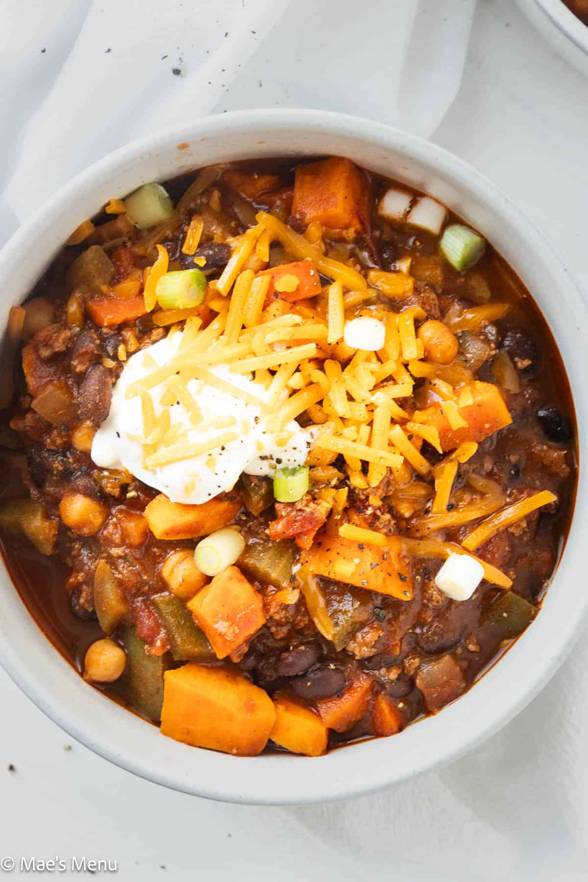 A close-up overhead shot of a bowl of bison chili topped with cheese and sour cream.