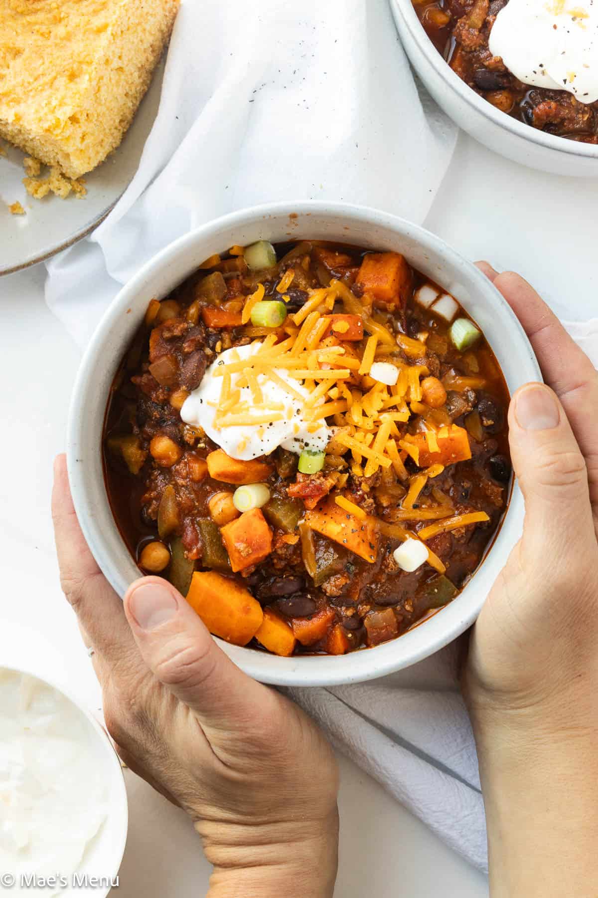 Two hands grabbing a bowl of bison chili on the counter.
