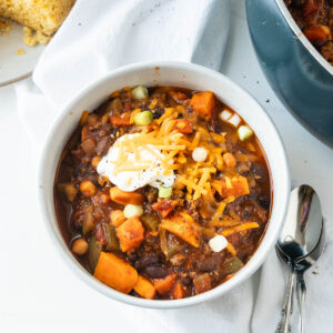 A bowl of bison chili on the counter with spoons and cornbread on the side.