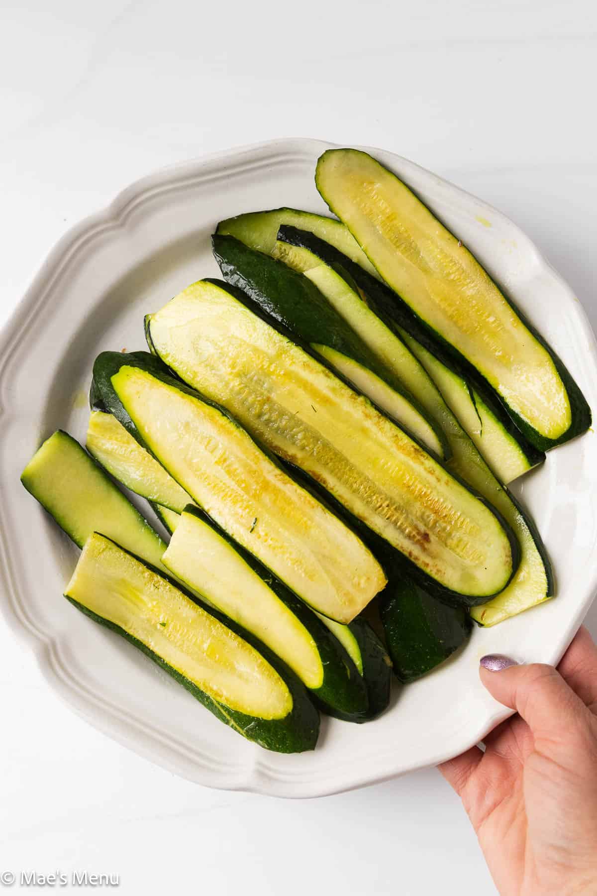An overhead shot of a hand grabbing a plate of browned zucchini planks.