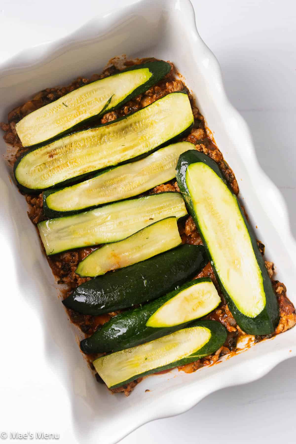 A pan of sauce with browned zucchini slices on top.