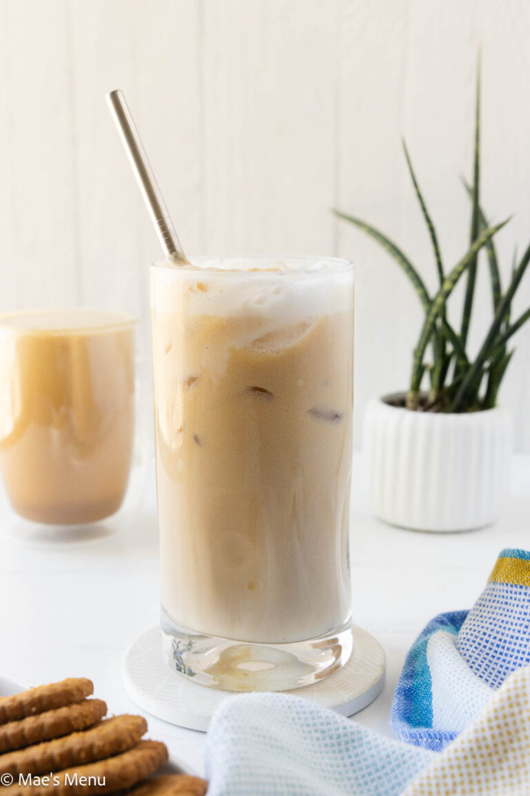 A side shot of a glass of iced protein coffee with a mug of hot protein coffee in the background.
