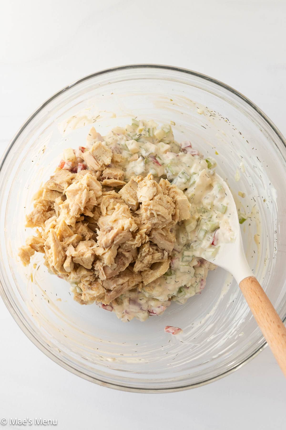 Adding flaked tuna to the bowl of the tuna pasta salad dressing with veggies.
