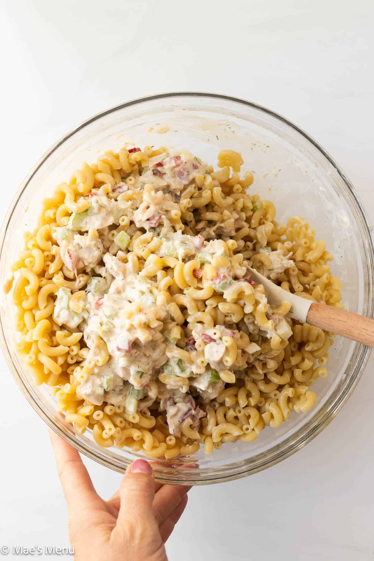 Two hands stirring the bowl of tuna pasta salad.