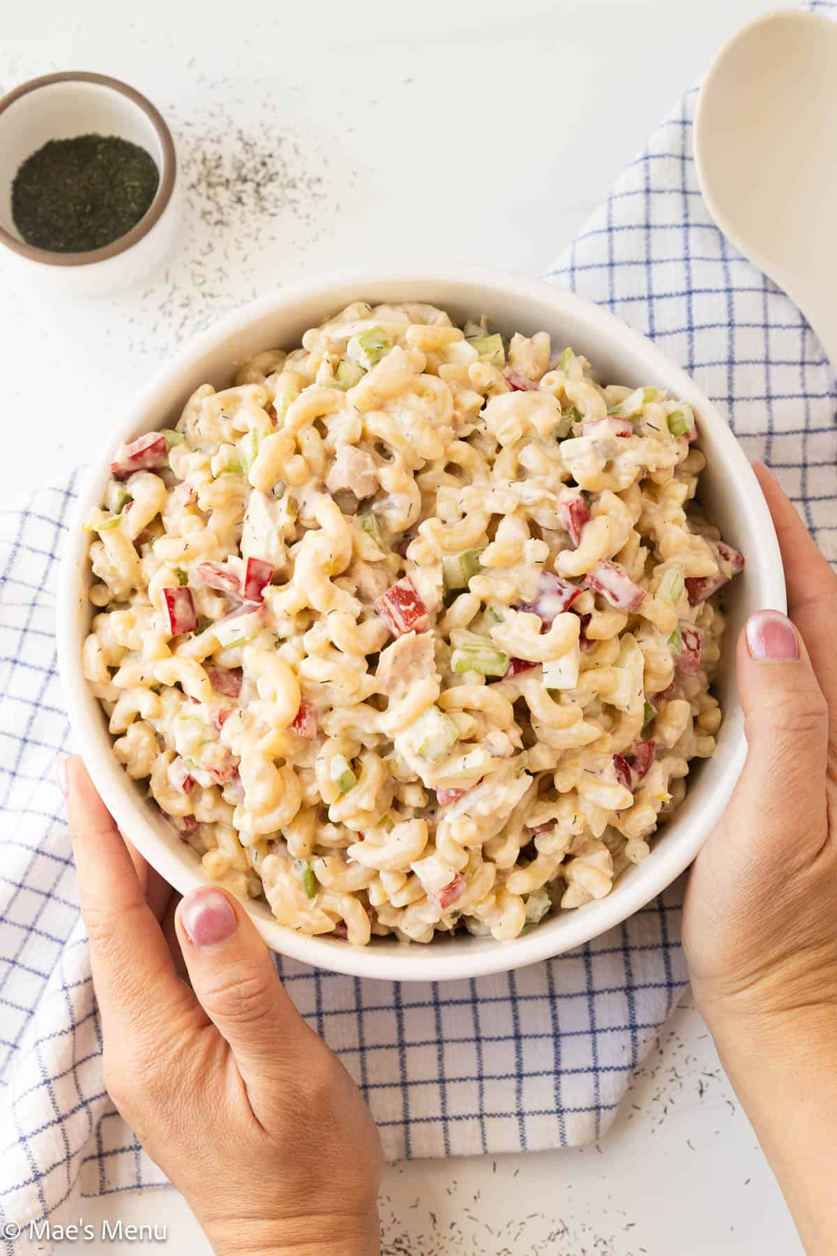 An overhead shot of two hands holding a serving bowl of tuna pasta salad.