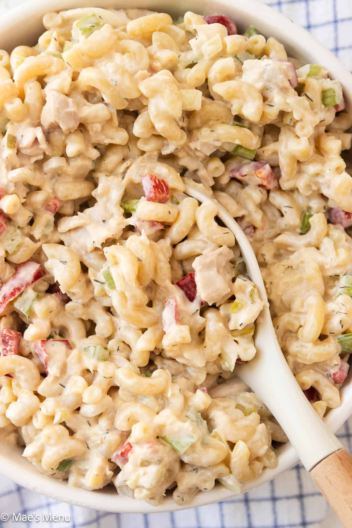 A locse-up shot of a bowl of tuna pasta salad with a serving spoon in it.