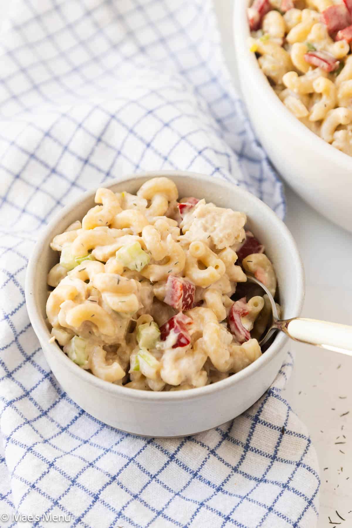 A close-up shot of a small bowl of tuna pasta salad with a spoon.