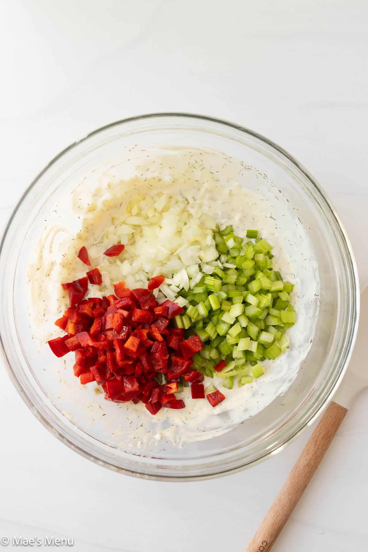 An overhead shot of a bowl of tuna pasta salad dressing with chopped bell pepper, onion, and celery.