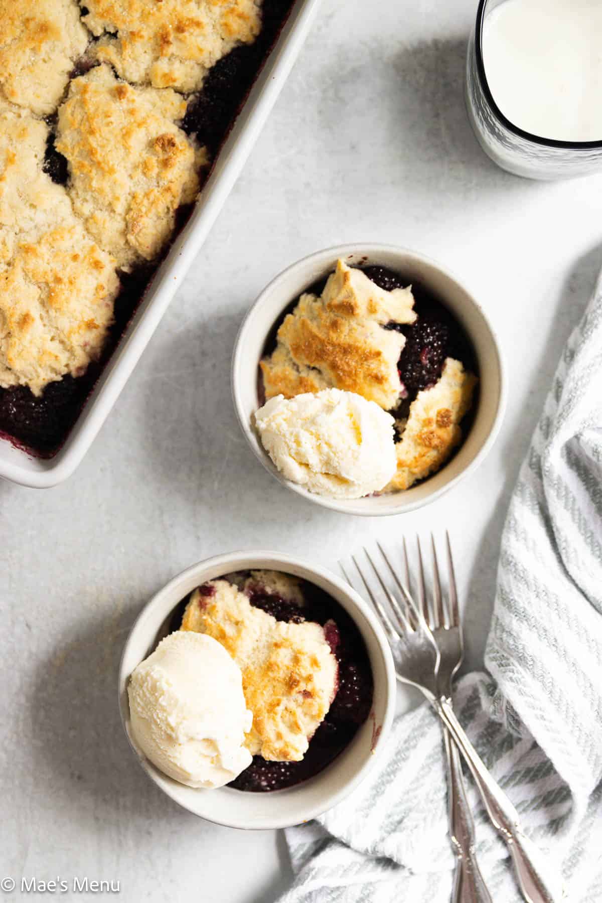 An overhead shot of two bowls of blackberry cobbler topped with ice cream.